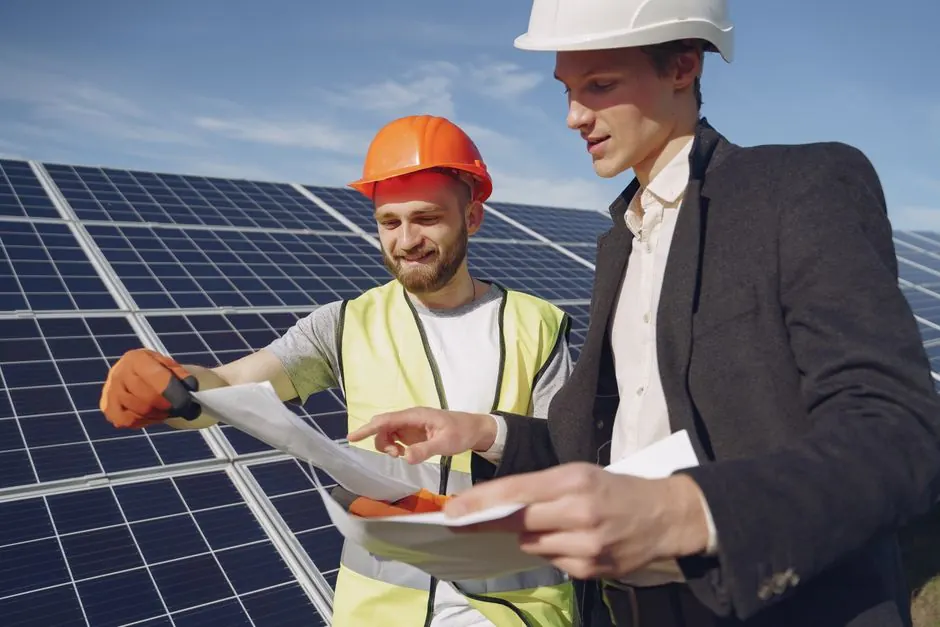 Low angle of young engineer and businessman in hardhats discussing project details against solar energy station